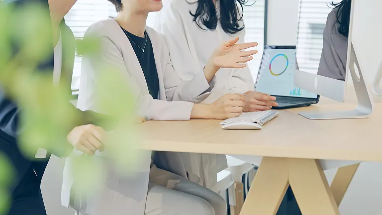 ノートパソコンのキーボードを打つ手元と、デスクに置かれたスマートフォン（実務完遂力・ハンズオンでの業務遂行をイメージ）